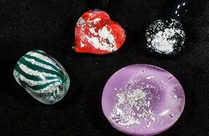 Assorted colorful memorial jewelry pieces on a dark background, with small ash inclusions visible inside the resin.
