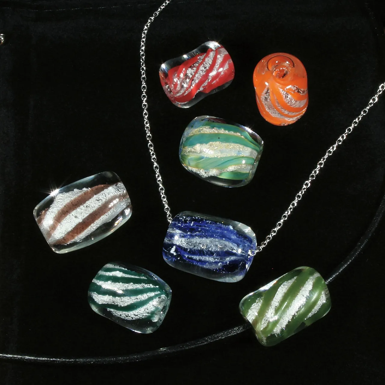 Glass bead and necklace display with striped and swirled beads in red, orange, green, blue, and clear tones on black velvet.
