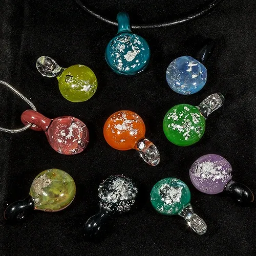 Assorted glass memorial pendants in multiple colors (red, green, blue, purple, orange) displayed on black fabric.