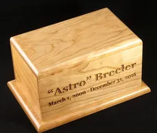 Close-up of a personalized wooden pet urn with an engraved name and dates on the front.