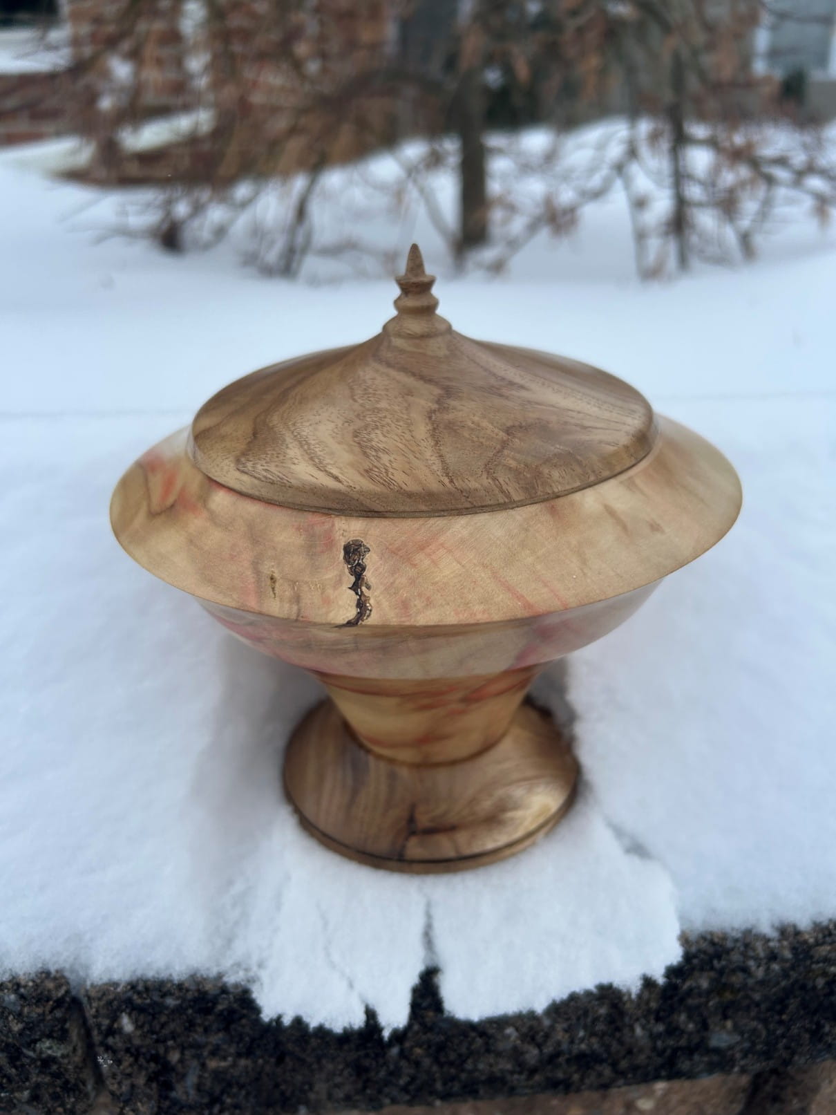Turned wooden lidded urn on a pedestal base, shown outside on snow.